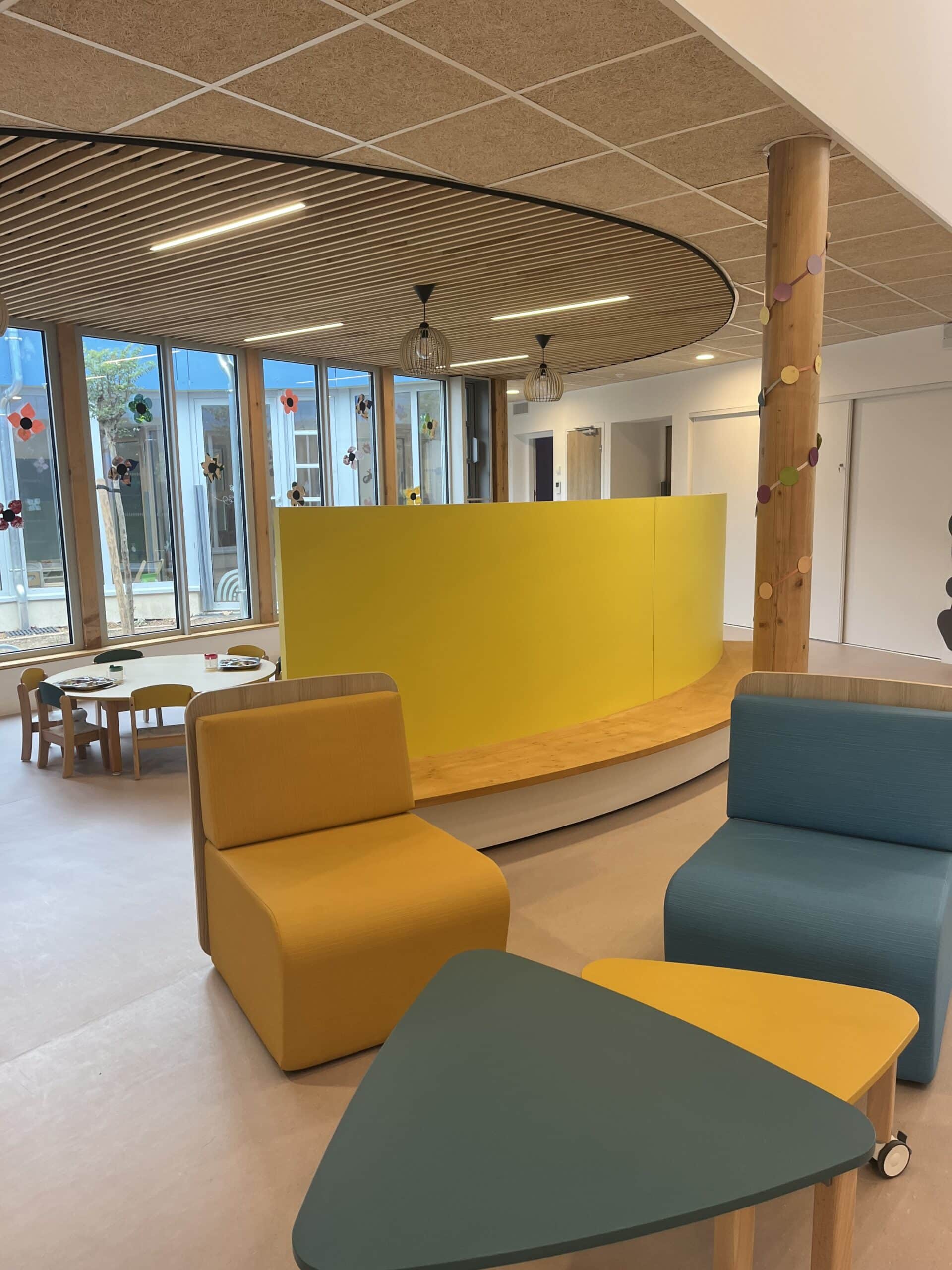 Aménagement intérieur d'une crèche moderne avec mobilier coloré, mur jaune courbé et coin repos lumineux.