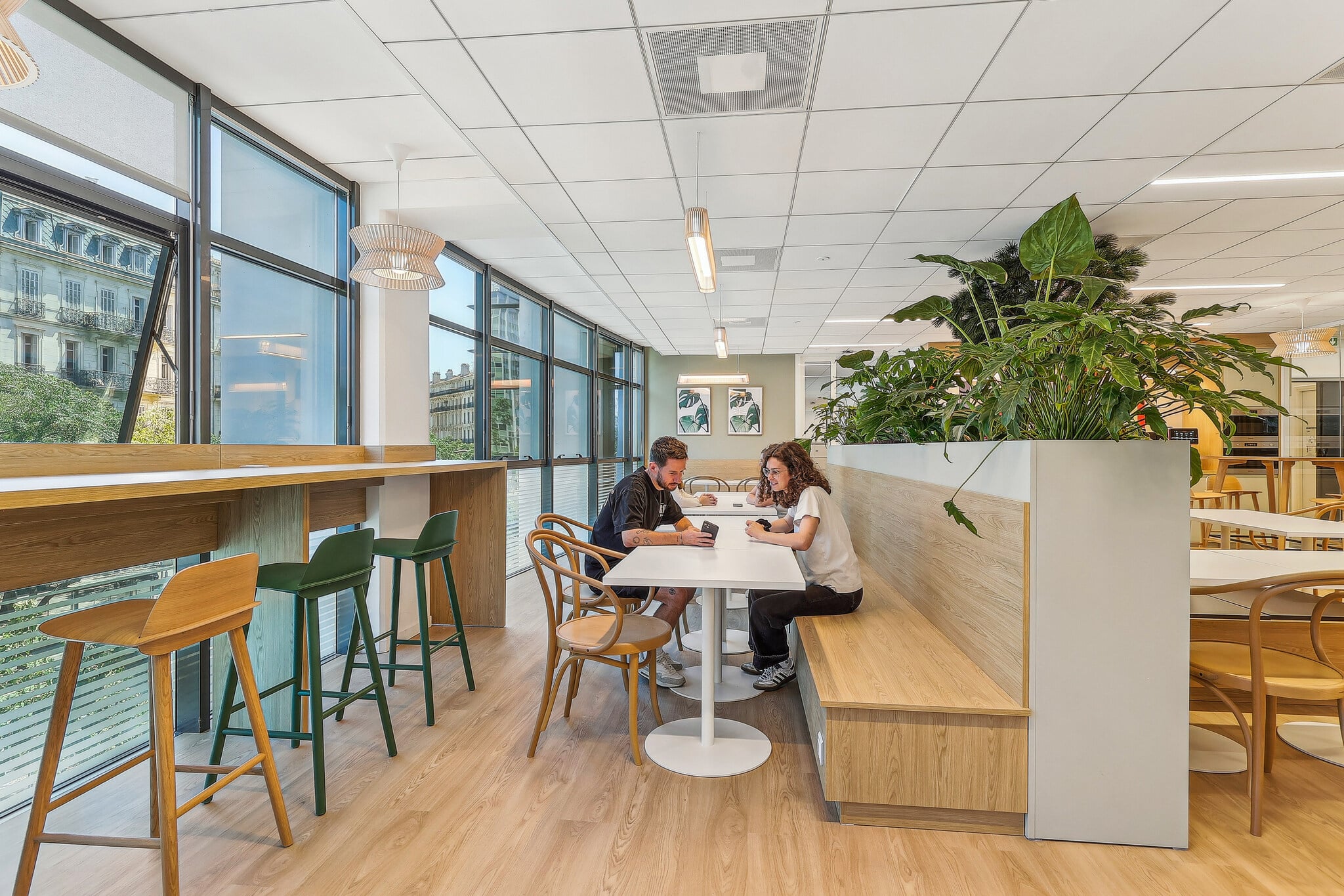 Espace détente bureau moderne avec design bois, plantes vertes et employés profitant de la vue urbaine.