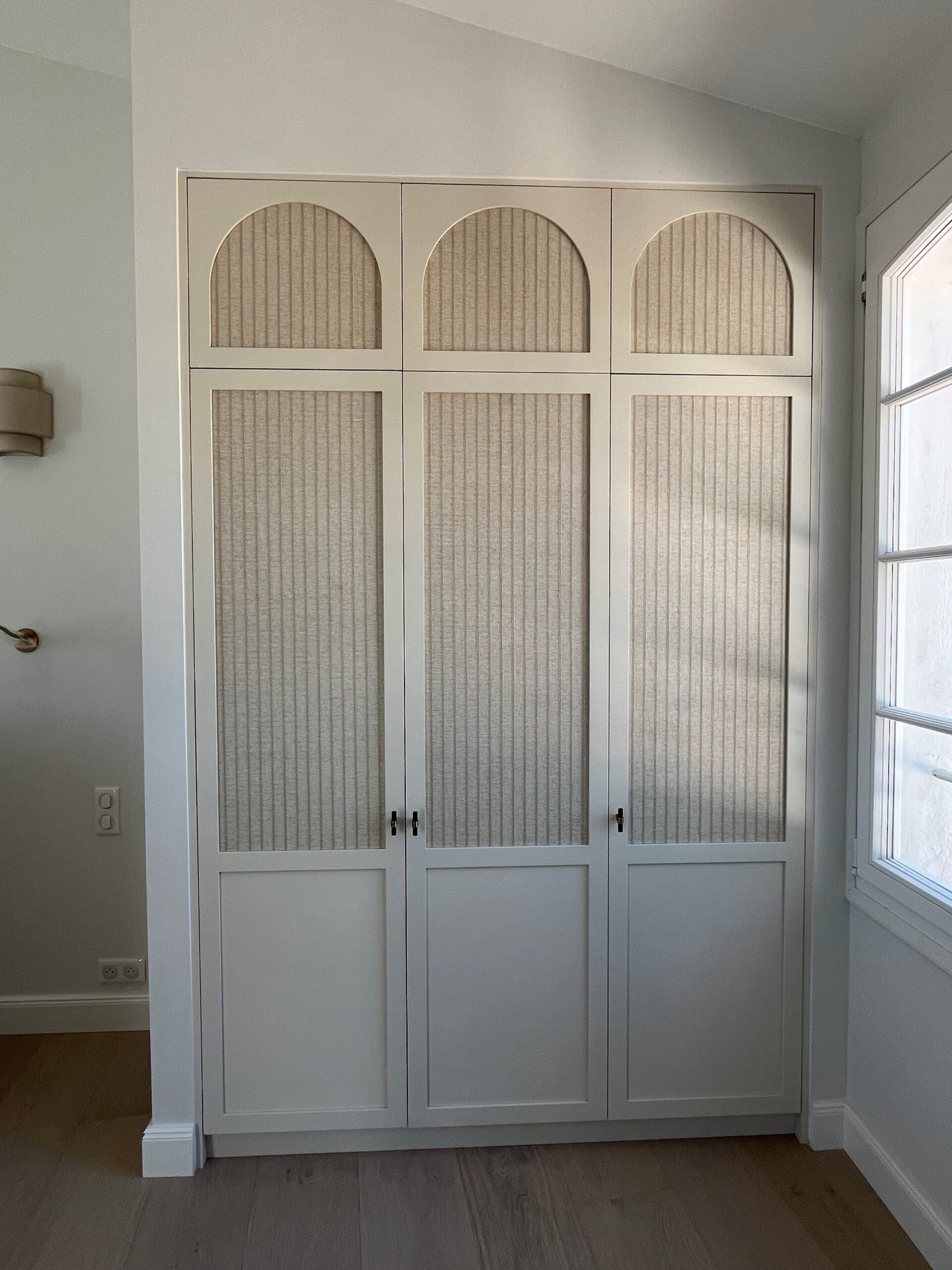 Armoire encastrée trois portes blanc cassé avec panneaux texturés et arches de style contemporain chic.