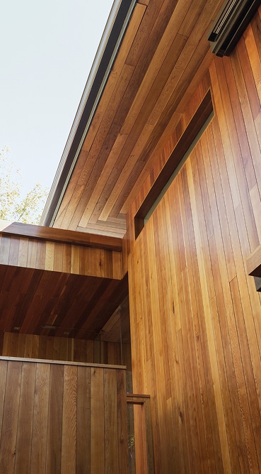 Bardage en bois clair et foncé avec plafond en lames de bois orientées différemment sous un ciel clair, architecture moderne.