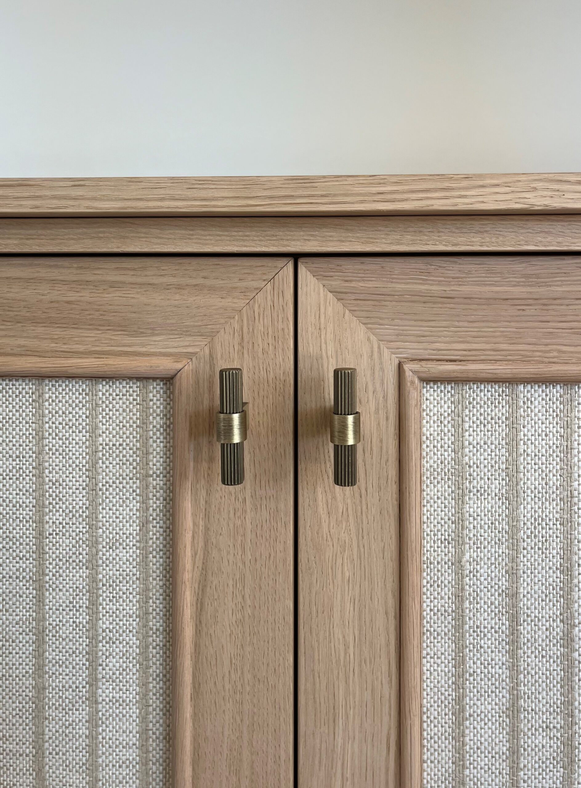 Buffet en bois clair avec panneaux texturés et boutons de meuble en laiton vieilli cannelé.