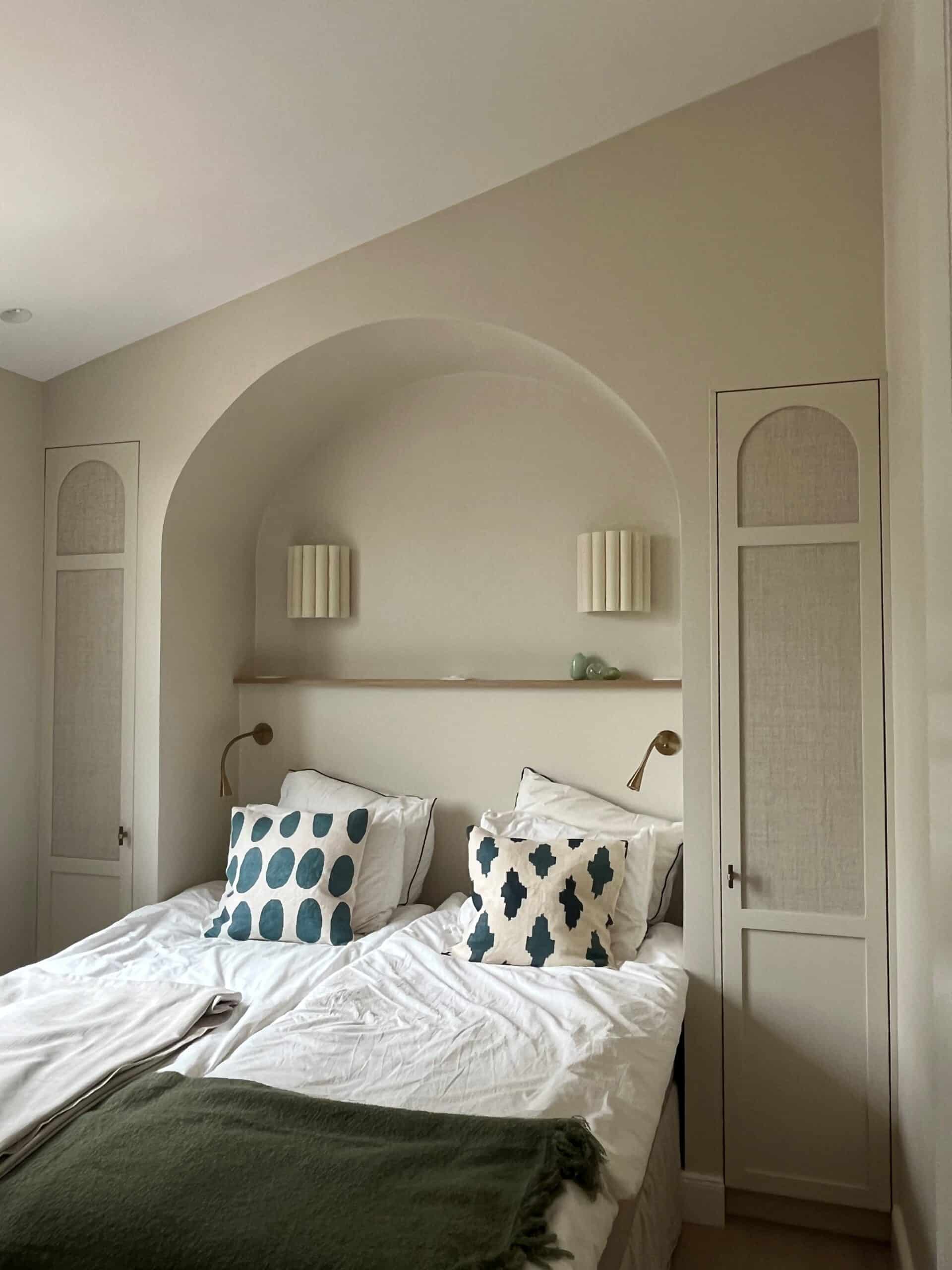 Alcôve en arche beige au-dessus d'un lit avec coussins bleus et placards encastrés dans une chambre minimaliste.