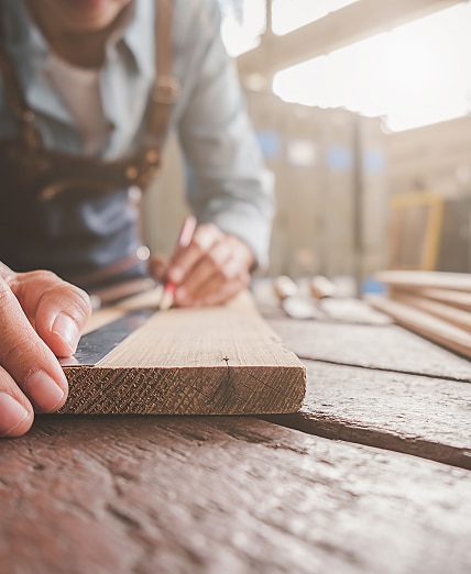 Un menuisier utilise une règle métallique pour marquer une planche de bois sur un établi rustique, concentration professionnelle.