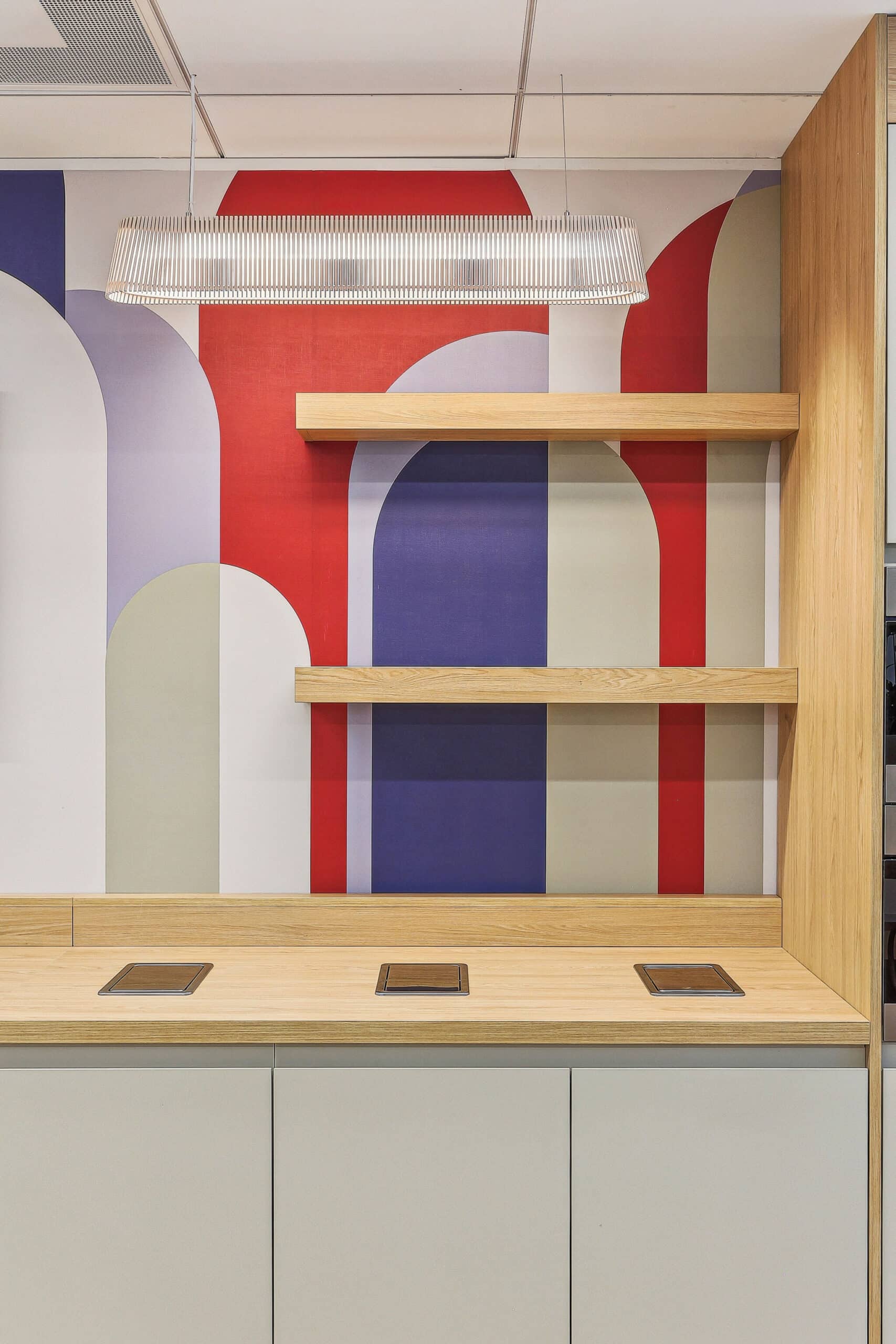 Étagères en bois sur mur mural géométrique coloré avec comptoir moderne et suspension linéaire design.