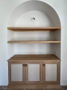 Niche murale arquée avec étagères flottantes en bois clair et meuble bas sur mesure à portes texturées.