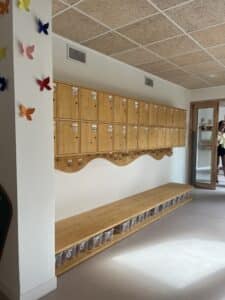 Vestiaire scolaire avec casiers en bois nominatifs, banc de rangement et papillons décoratifs au mur.