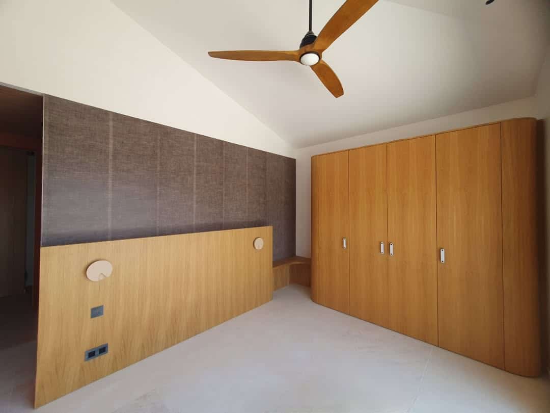 Chambre moderne avec plafond cathédrale, ventilateur bois, grande tête de lit en bois clair et placard intégré assorti.