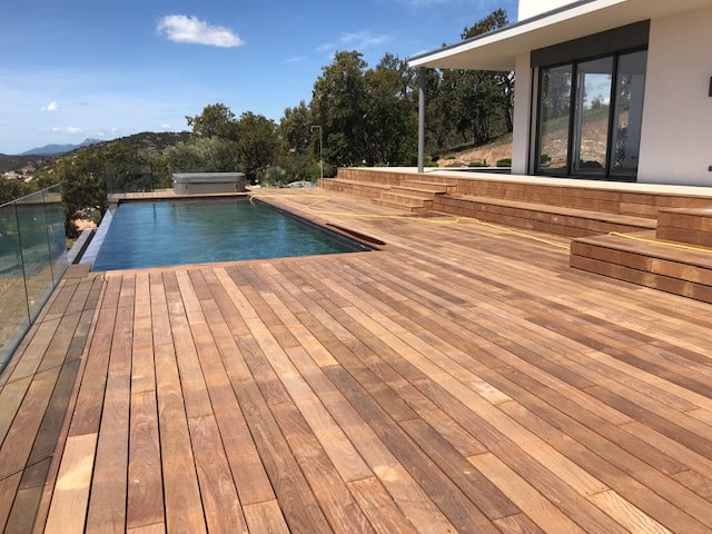 Terrasse en bois avec piscine à débordement de luxe Terrasse en bois exotique avec piscine à débordement et vue panoramique sur les montagnes par temps ensoleillé.
