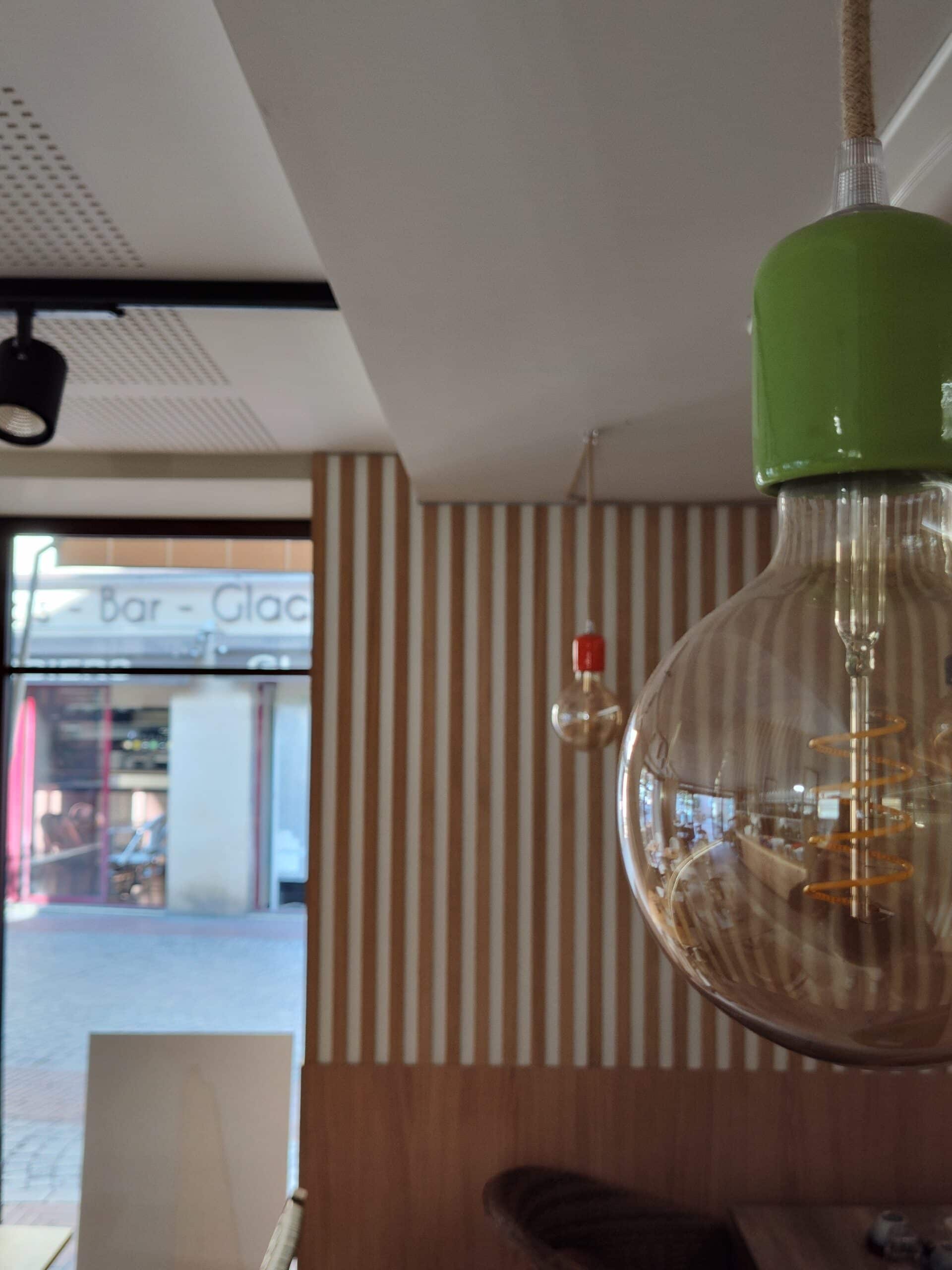 Ampoule à filament spirale avec douille verte dans un café, vue sur un mur rayé et une enseigne Bar - Glac.