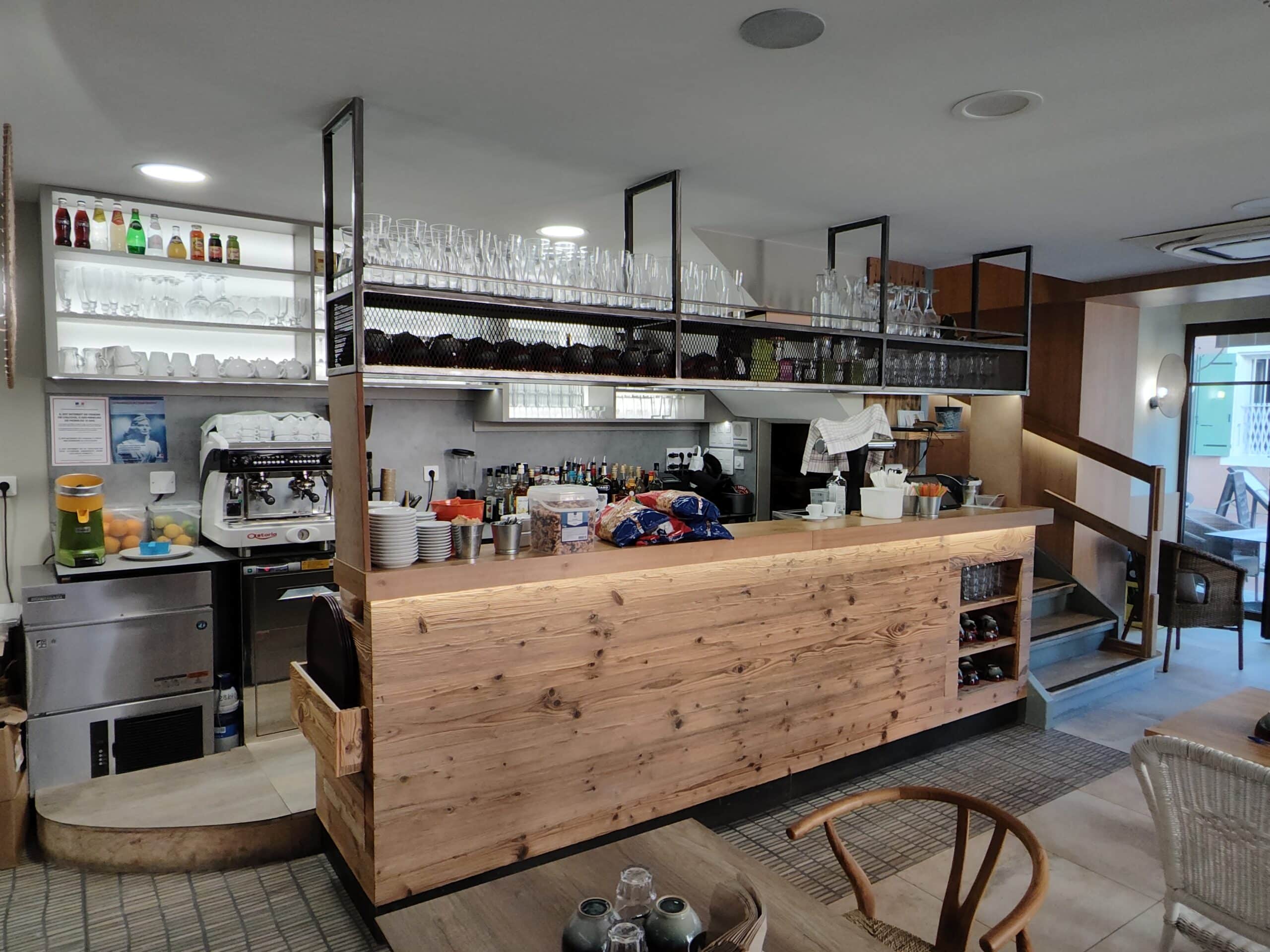Comptoir de bar en bois massif avec machine expresso Astoria et verres suspendus dans un café moderne.