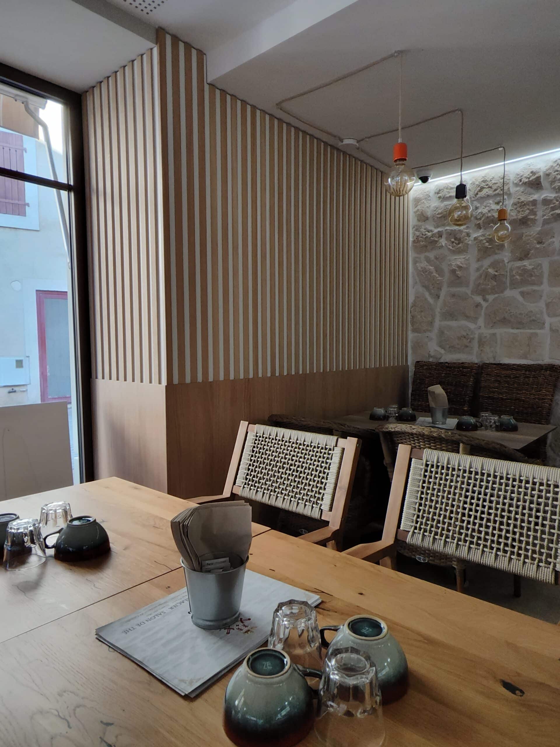 Intérieur de salon de thé moderne avec tables en bois, mur en pierre et menu Glacier Salon de Thé.