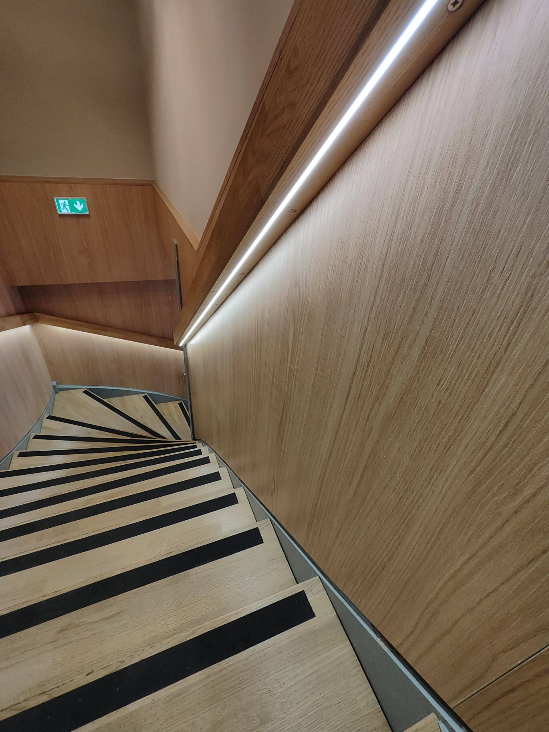 Escalier tournant en bois avec bandes antidérapantes, rampe lumineuse LED intégrée et signal de sortie de secours.