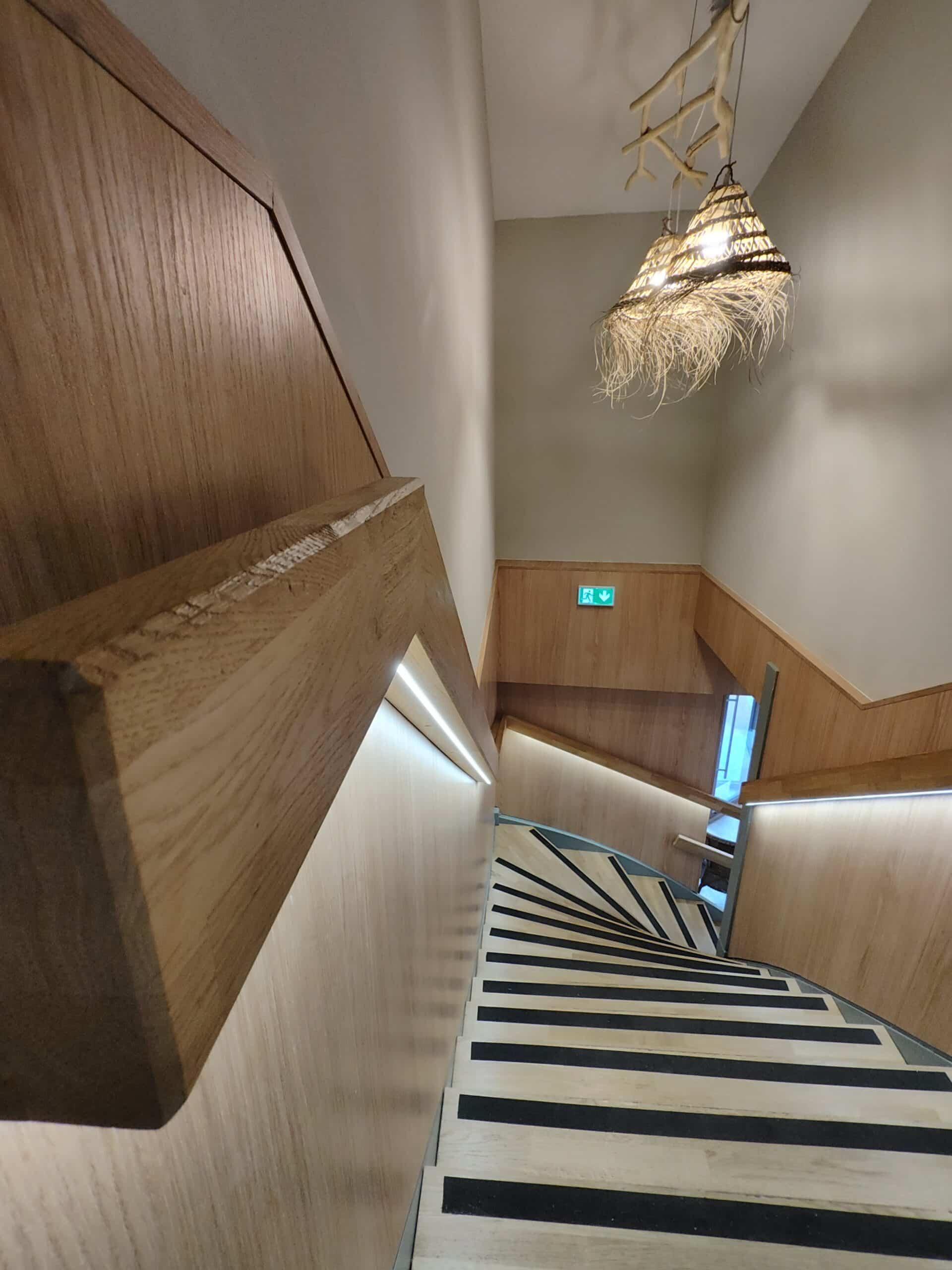 Escalier en bois design avec éclairage LED intégré, marches antidérapantes et luminaire rustique suspendu.