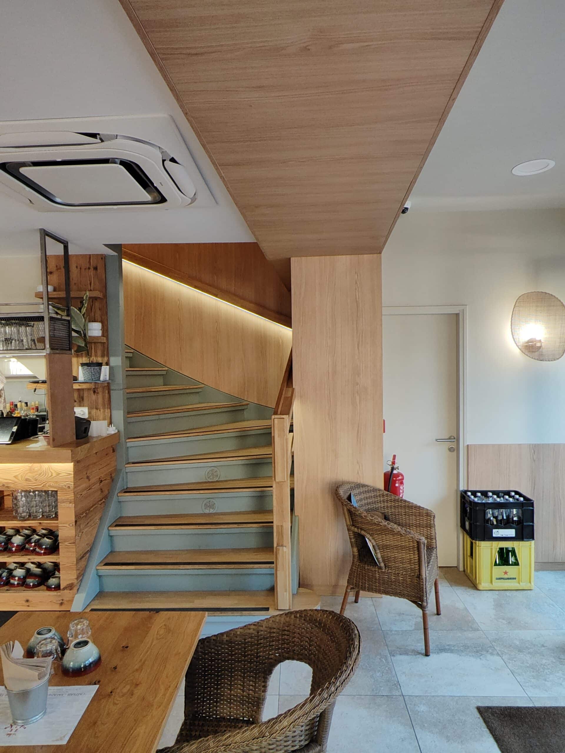 Escalier en bois avec éclairage LED, chaises en osier et table dans un intérieur de restaurant moderne et chaleureux.